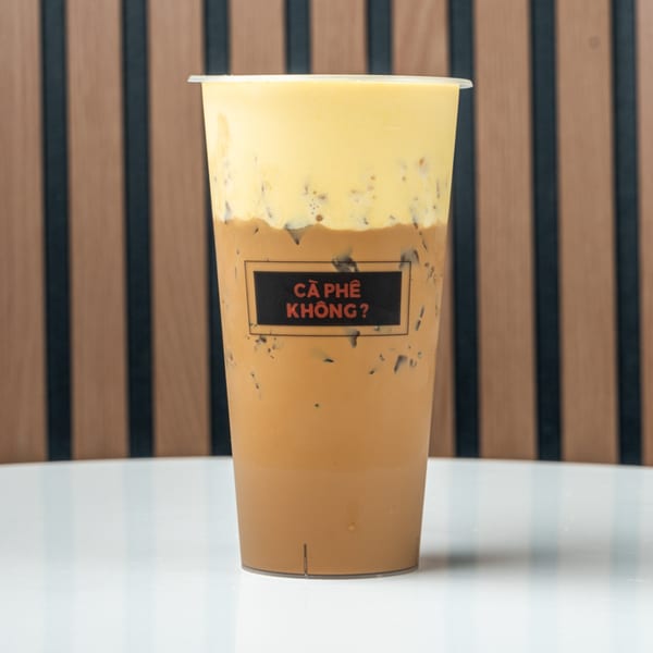 Iced coffee with a thick layer of yellow foam on top, with a black label on the cup.