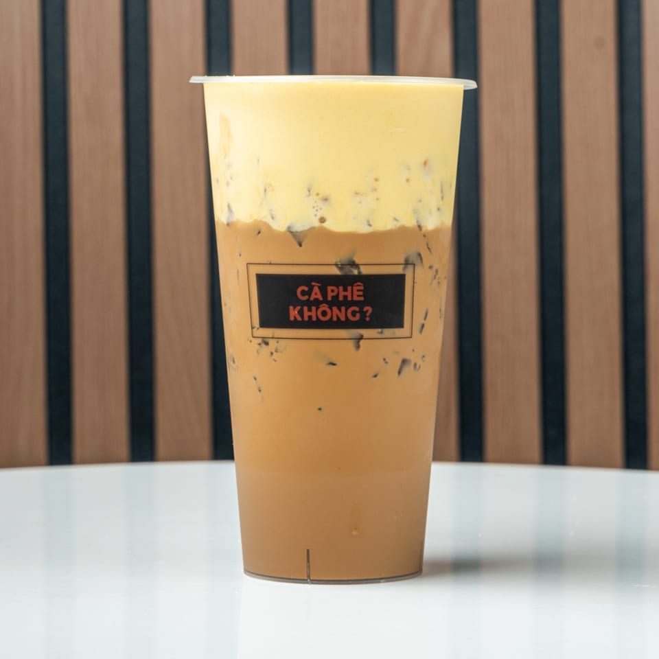 Iced coffee with a thick layer of yellow foam on top, with a black label on the cup.