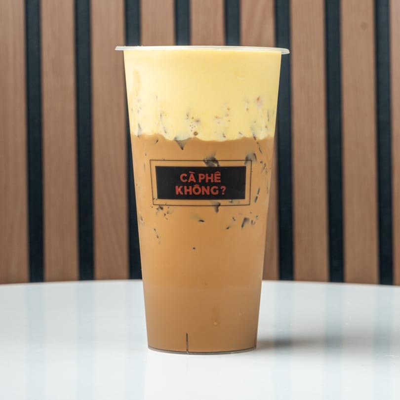 Iced coffee with a thick layer of yellow foam on top, with a black label on the cup.