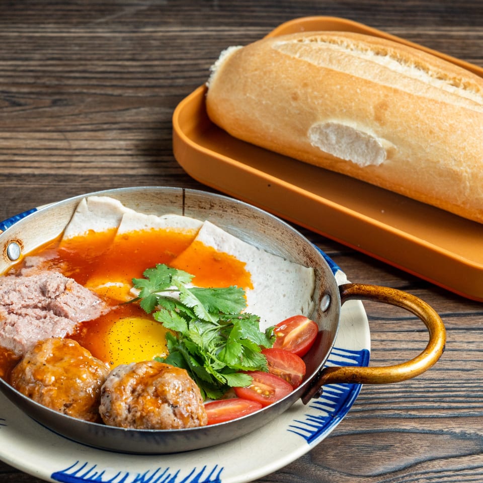 Banh Mi Ong Beo's Vietnamese breakfast skillet with meatballs, pate, egg, and cilantro, served with a baguette.