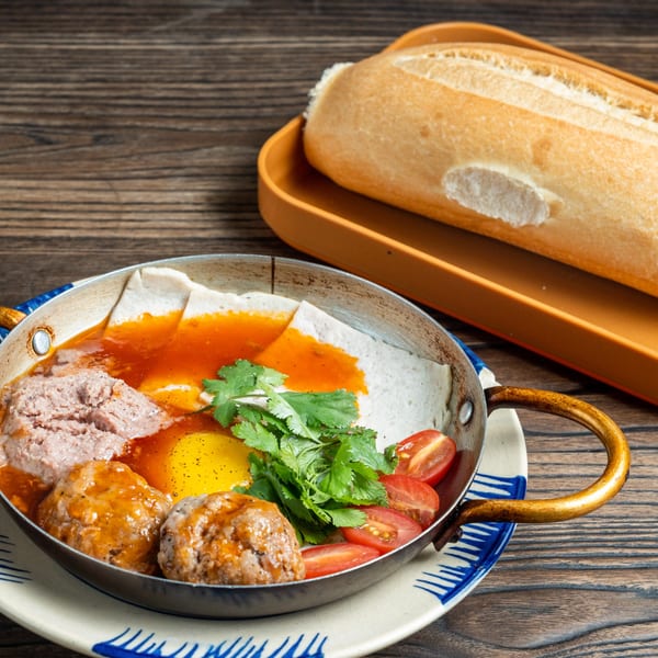 Banh mi chao with meatballs, pate, fried egg, cilantro, tomatoes, and a baguette.