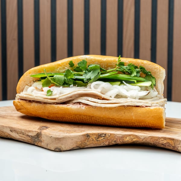 A Banh Mi Ong Beo sandwich with meat, cilantro, and onions on a wooden board.