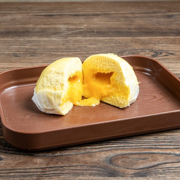 A steamed bun, cut in half, revealing a gooey yellow custard filling on a brown tray.