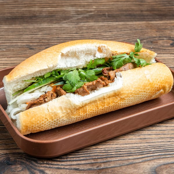 A Banh Mi Ong Beo sandwich filled with meat, cilantro, and vegetables on a brown tray.