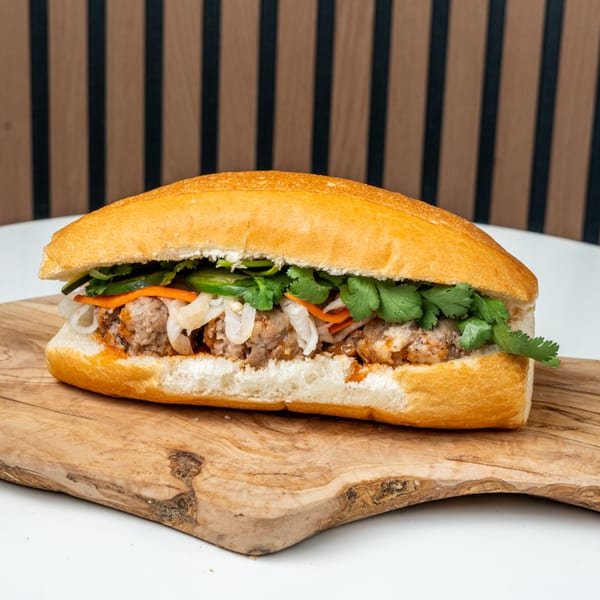 A Banh Mi Ong Beo sandwich with meatballs, pickled vegetables, and cilantro on a wooden board.