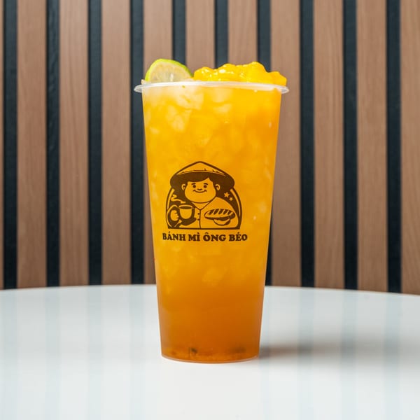 A Banh Mi Ong Beo mango drink with lime and mango chunks on a white table.
