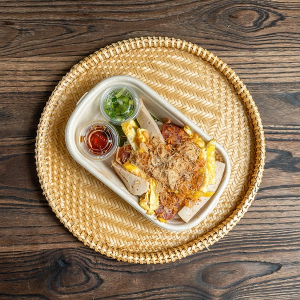 Banh Mi Ong Beo's Vietnamese dish with meat, egg, and shredded pork, served with sauces on a woven tray.
