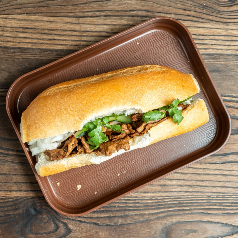 A Banh Mi Ong Beo sandwich with meat, cilantro, and onions on a brown tray.