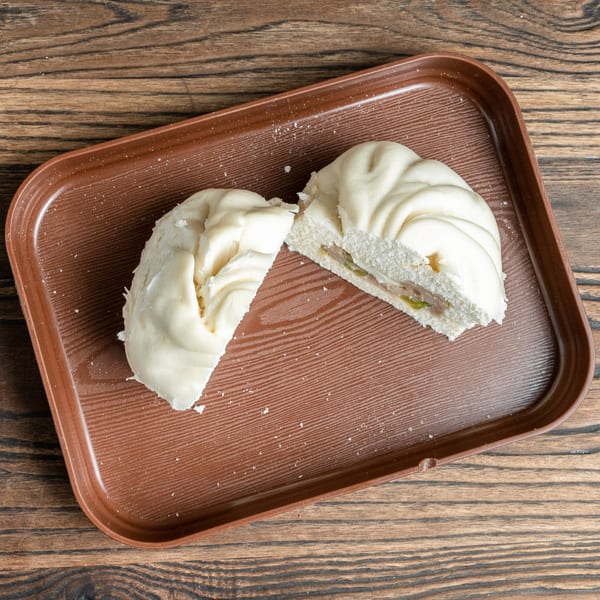 Two halves of a steamed bun (Banh Bao) with meat filling on a brown tray.