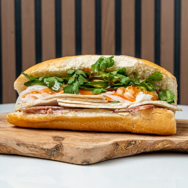 A Banh Mi Ong Beo sandwich filled with meat, pickled vegetables, and cilantro on a wooden board.